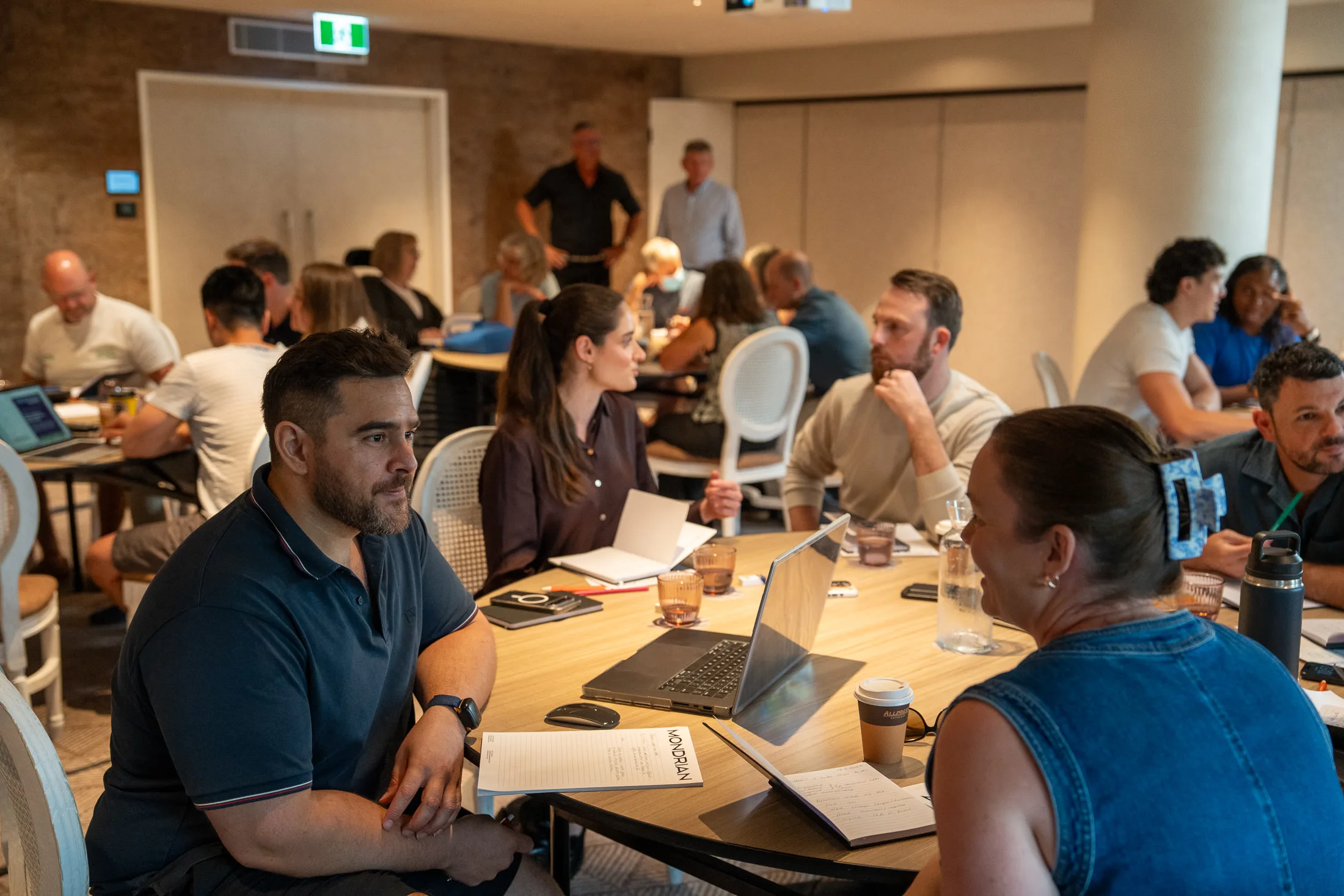 A wide view of the Hive Practice colony — practice owners gathered around tables in a working session